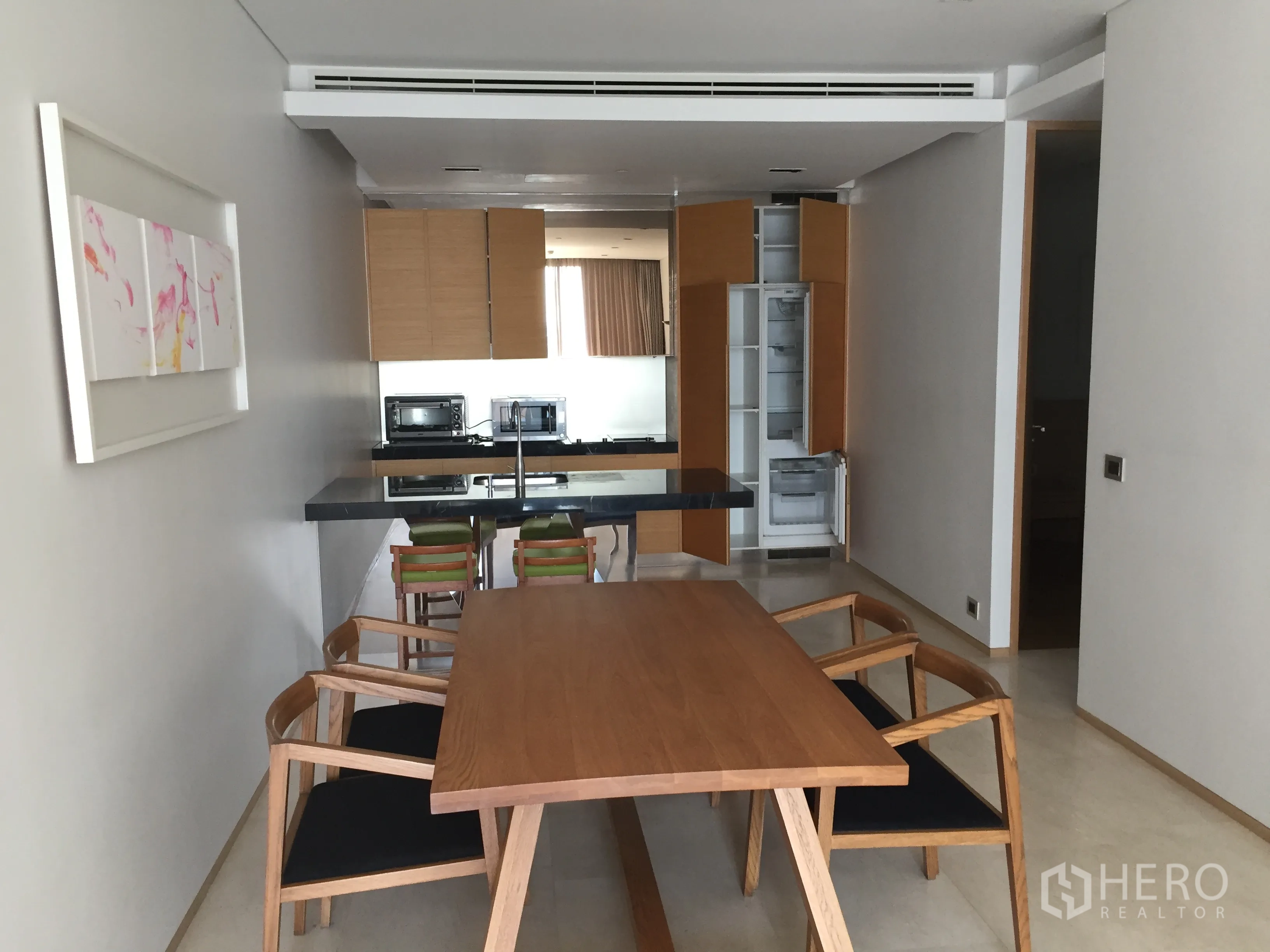 Condominium for rent in Bang Rak, Bangkok - Dining area with wooden table and chairs facing a sleek open kitchen with island and built-in appliances.