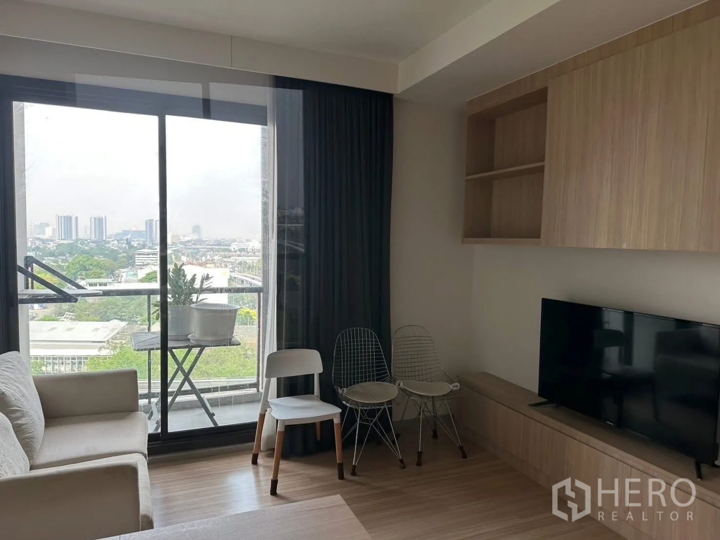 公寓 出租在Chatuchak, Bangkok - 采光充足的客厅，连接阳台与城市景观，带电视柜和木质收纳柜。