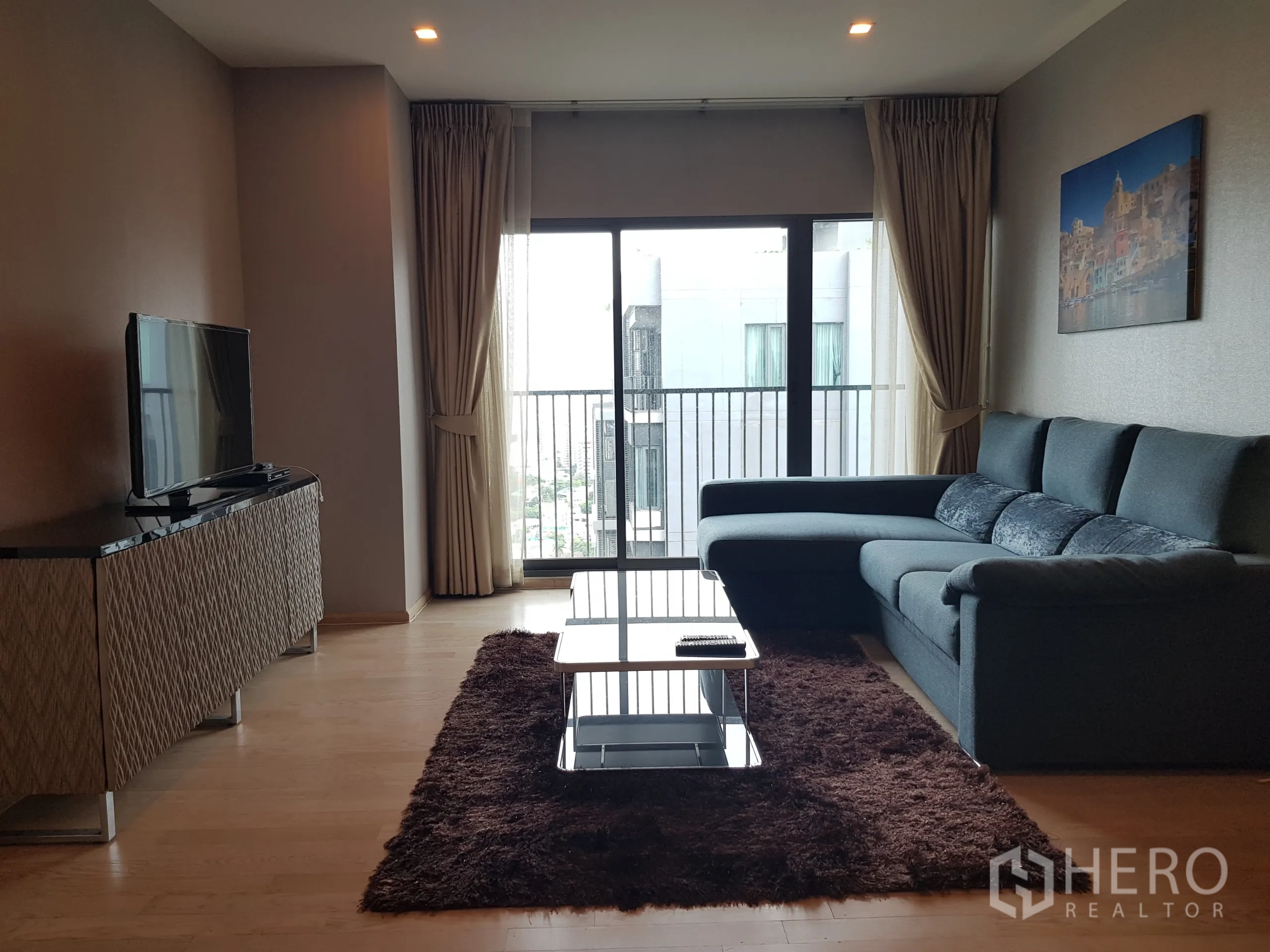 Condominium for rent in Khlong Toei, Bangkok - Spacious lounge with sectional sofa facing TV and full-height glass doors.