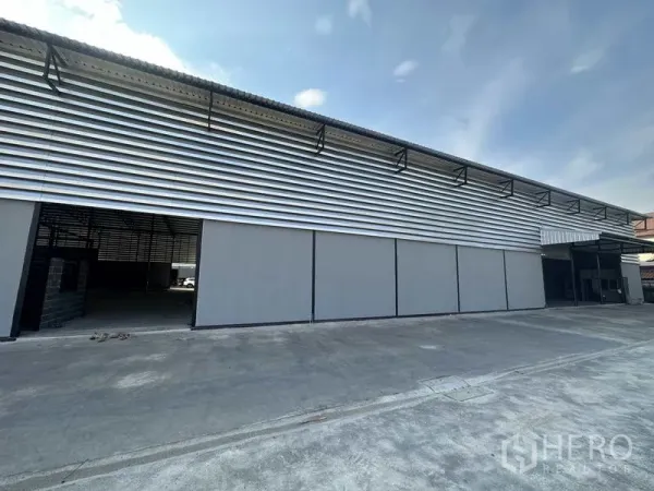 Warehouse for rent in Lam Luk Ka, Pathum Thani - Side facade with horizontal metal cladding and multiple sliding doors along the loading frontage.