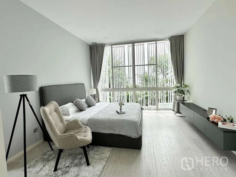 Detached House for rent or sale in Bang Phli, Samut Prakan - Bright bedroom with large windows, gray bed and minimalist decor.
