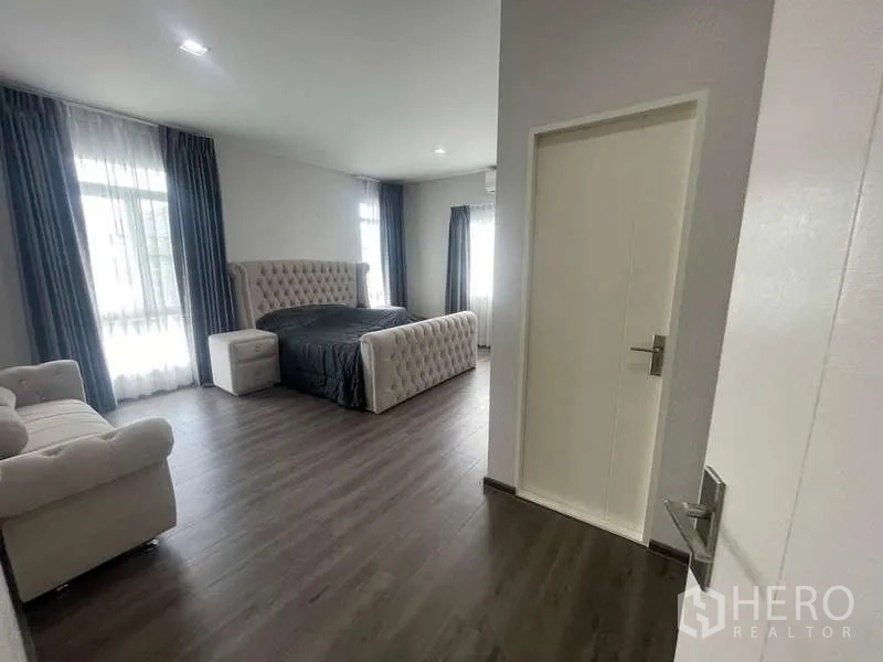 Detached House for rent or sale in Bang Bua Thong, Nonthaburi - Spacious master bedroom with dark wood flooring, tufted bed, and large curtained windows.