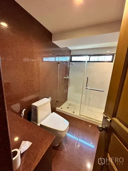 Condominium for rent in Bangkok - Bathroom with glass-enclosed shower, white sanitary ware and marble-toned walls.