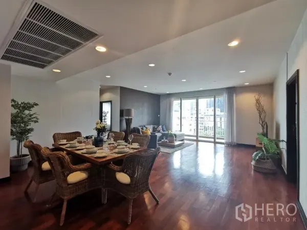 Condominium for rent or sale in Khlong Toei, Bangkok - Open-plan living and dining area with hardwood flooring, rattan dining set, and wide windows to the balcony with city views.