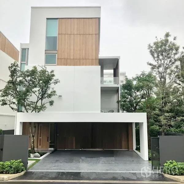 Detached House for rent in Saphan Sung, Bangkok - Contemporary three-storey detached house exterior with wood-and-white facade, trees and covered carport.