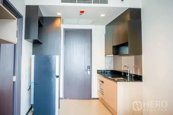 公寓 出售在Watthana, Bangkok - 紧凑厨房，黑色台面、洗槽、微波炉与冰箱，位于入户门旁