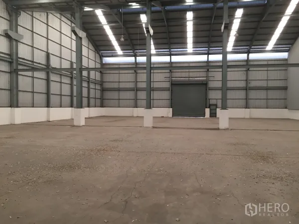 Factory for rent in Khlong Luang, Pathum Thani - Spacious warehouse interior with a high roof, skylights, and a large roller door.
