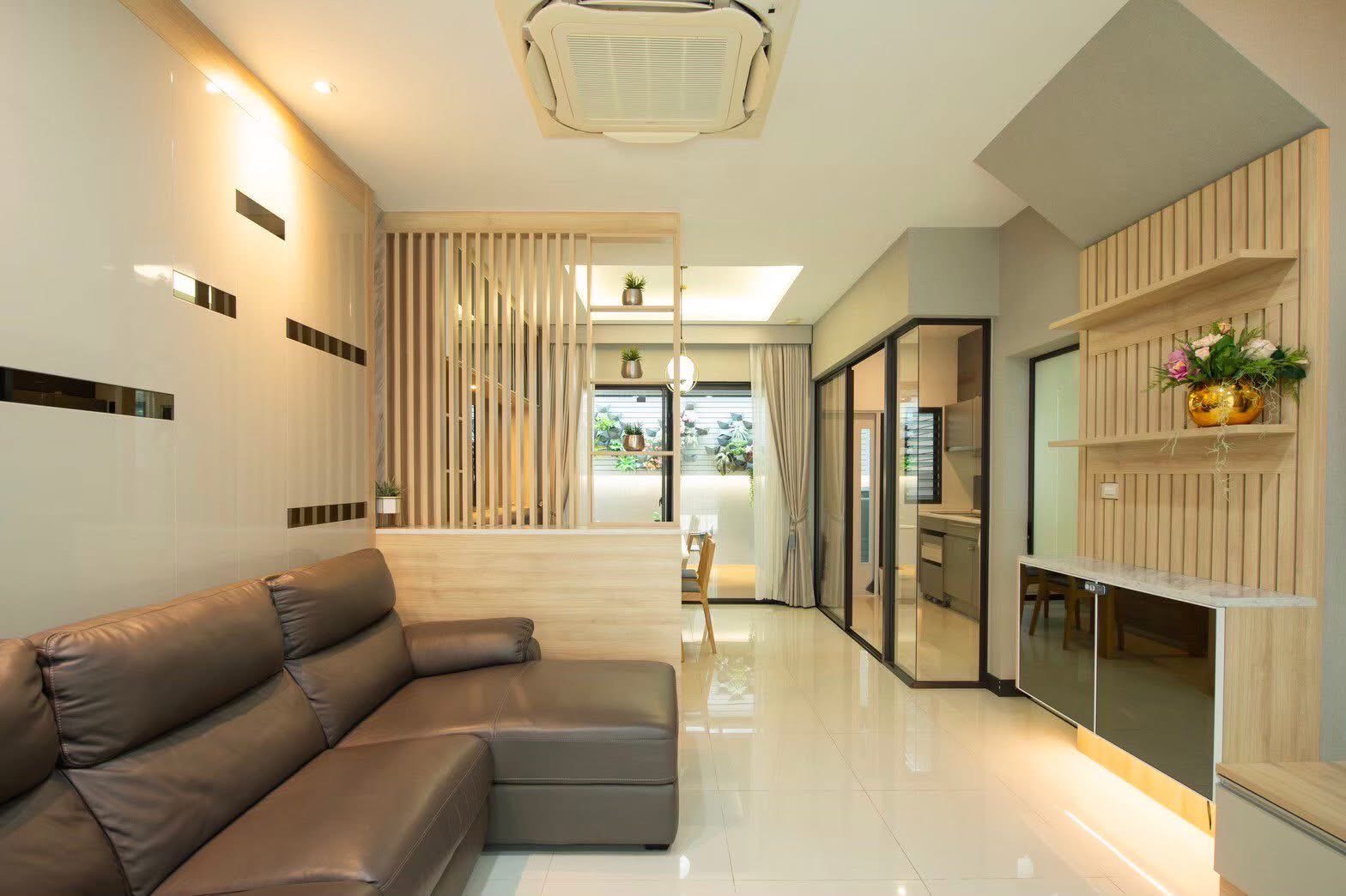 Townhouse for rent or sale in Lat Phrao, Bangkok - Open-plan living area with leather sectional sofa, wood slat partition and glass kitchen doors.