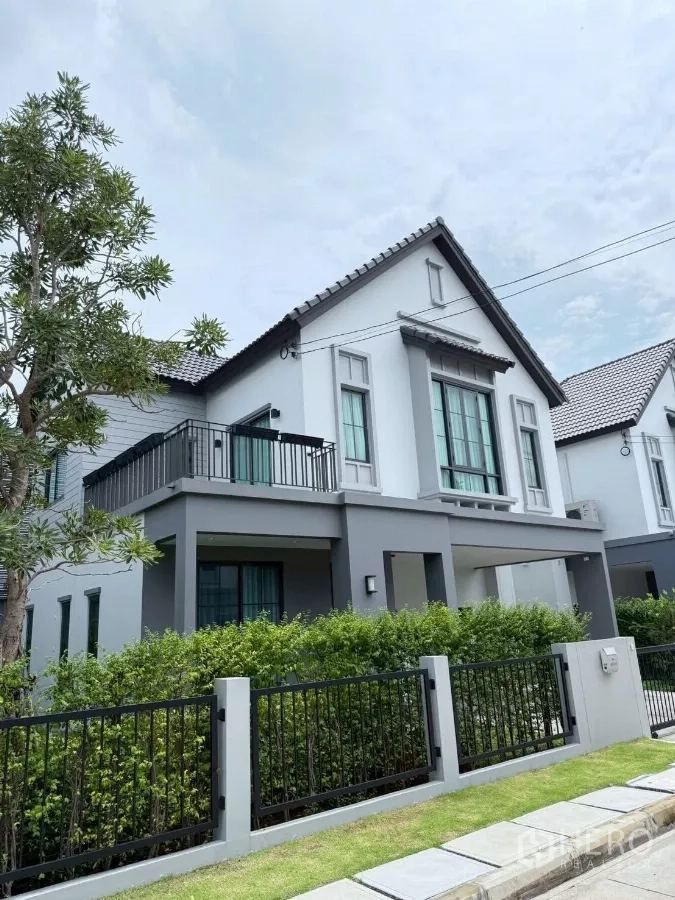 Detached House for rent in Lat Krabang, Bangkok - Corner angle of the house showing balcony, black metal fence and landscaped hedges.
