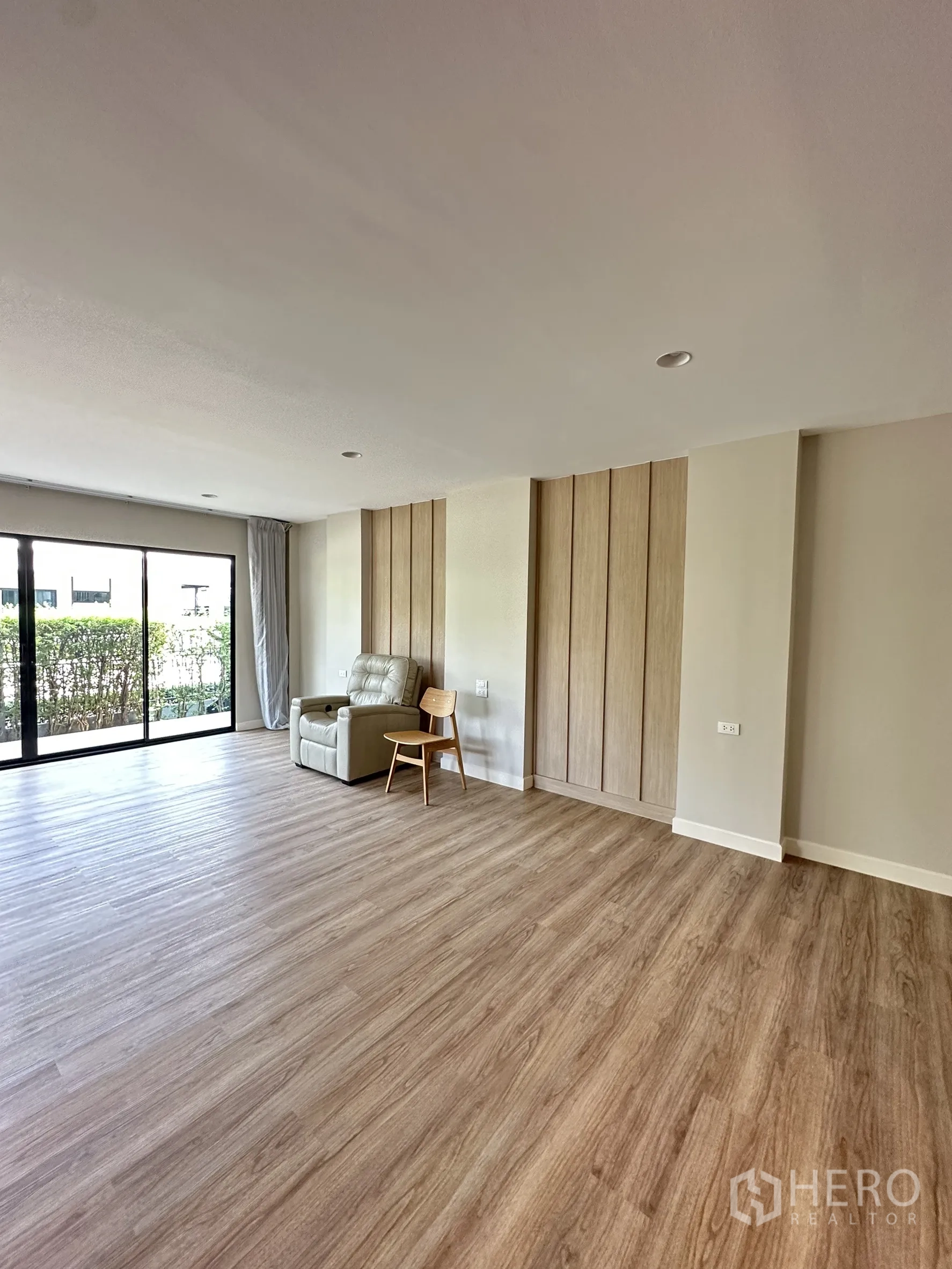 Detached House for sale in Lam Luk Ka, Pathum Thani - Large ground-floor multipurpose room with wood-look flooring and garden view.