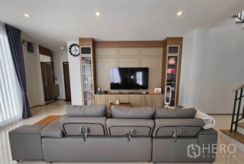 Detached House for rent or sale in Lat Krabang, Bangkok - Open living room with large sofa facing a media wall and built‑in cabinetry