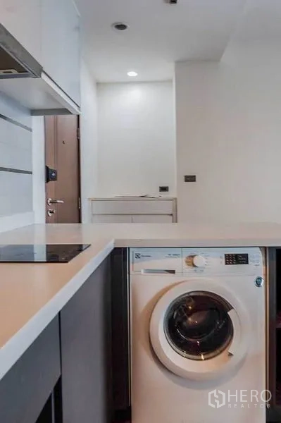 Condominium for rent in Khlong Toei, Bangkok - Front-loading washing machine built under the kitchen counter near the entry.