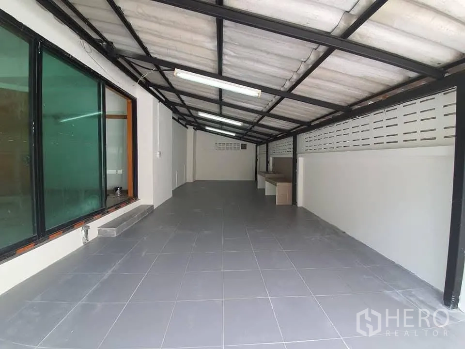 家庭办公室 for rent in Wang Thonglang, Bangkok - 带金属顶棚的室内车位，地面铺砖，旁侧为大片墨色玻璃窗。