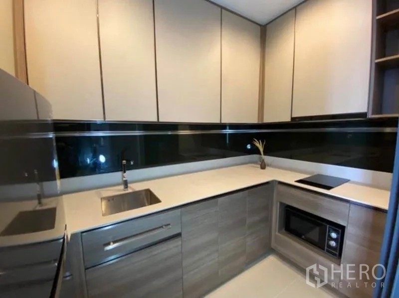 Condominium for rent or sale in Phaya Thai, Bangkok - U-shaped kitchen with upper cabinets, sink, cooktop and microwave.