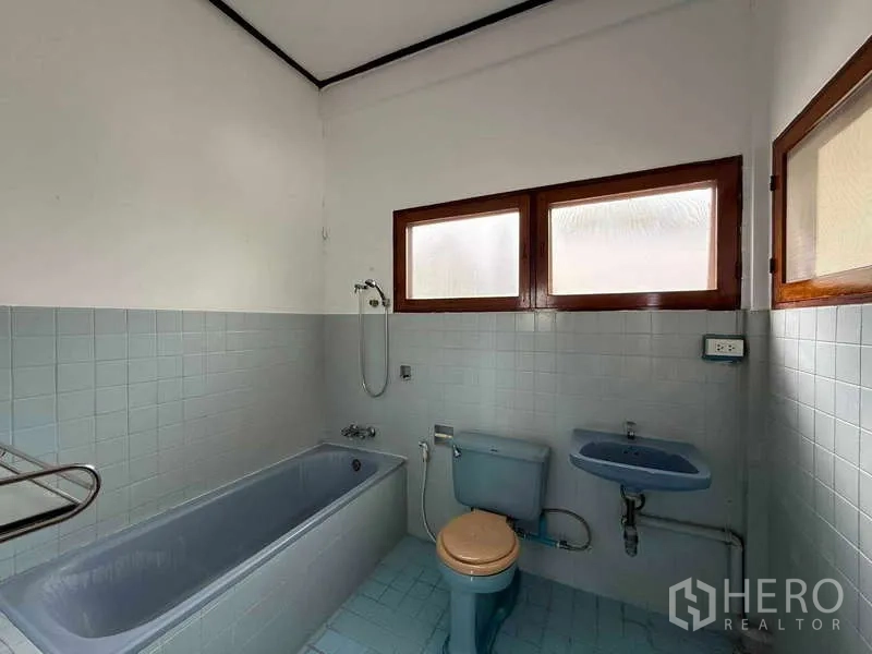 Detached House for rent in Watthana, Bangkok - Vintage bathroom with blue bathtub, toilet and sink beneath frosted windows.