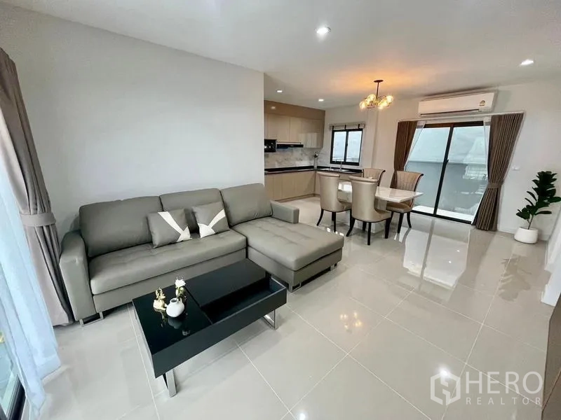 联排别墅 出租在Bang Phli, Samut Prakan - 邦披联排别墅的明亮开放式客餐厅，L 型沙发、石纹餐桌、米色厨房与推拉落地门。