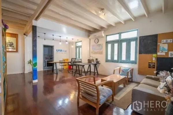 Detached House for rent in Khlong Toei, Bangkok - Open-plan living and work area with wooden floors, beamed ceiling, sofa set, and large windows.