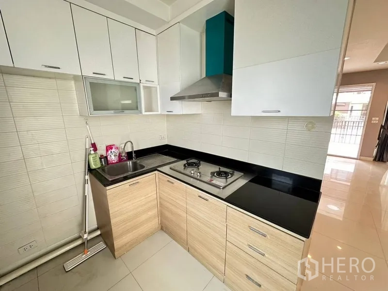 Townhouse for rent or sale in Phra Khanong, Bangkok - L-shaped kitchen with gas hob, cooker hood, black countertop, and white-wood cabinets.