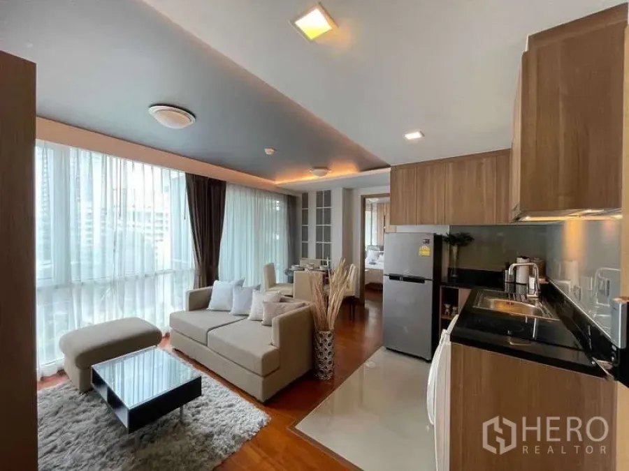 Condominium for sale in Watthana, Bangkok - Living area with sofa, ottoman, shag rug and galley kitchen with black stone countertop.