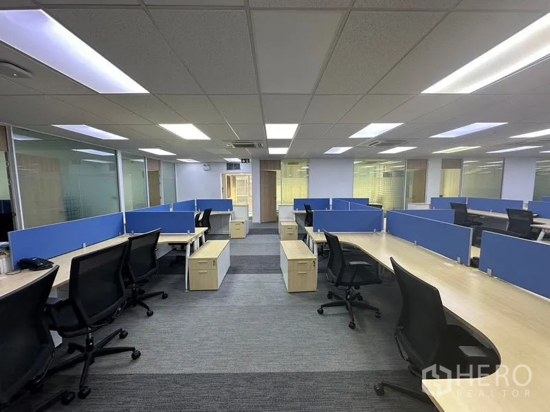 Office Space for rent - Open-plan workspace with blue-partition workstations, rolling chairs and suspended LED panels.