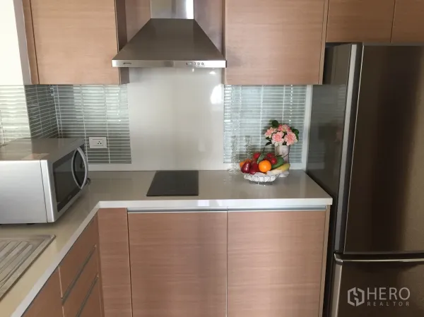Condominium for rent or sale in Khlong Toei, Bangkok - Modern kitchen with wood cabinets, stainless hood, glass tile backsplash and fridge.
