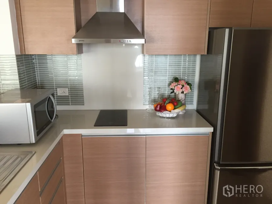 Condominium for rent or sale in Khlong Toei, Bangkok - Modern kitchen with wood cabinets, stainless hood, glass tile backsplash and fridge.