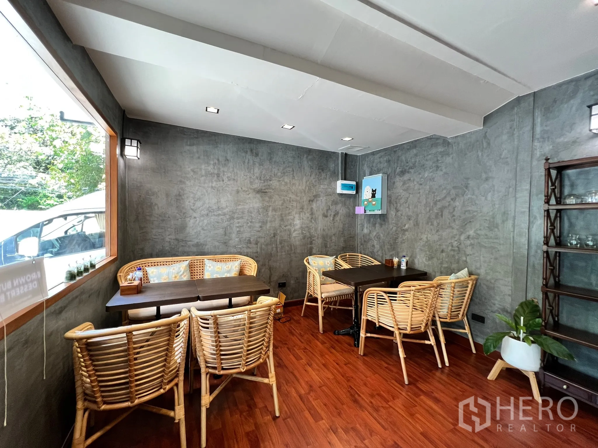พื้นที่ขายปลีก ให้เช่าในWatthana, Bangkok - โซนที่นั่งริมหน้าต่าง เก้าอี้หวาย ผนังคอนกรีตตกแต่ง พร้อมกระถางต้นไม้และชั้นวาง