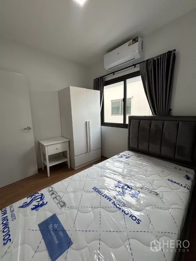 Townhouse for rent in Bang Phli, Samut Prakan - Single bedroom with wardrobe, bedside table and window air conditioner.