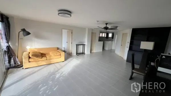 Condominium for sale in Wang Thonglang, Bangkok - Living room facing an open kitchen, with a yellow sofa by the window and multiple doors.