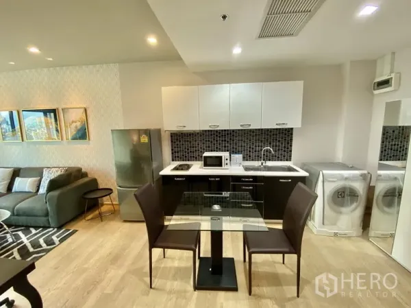 Condominium for rent in Bangkok - Compact kitchen with fridge, cooktop, microwave, sink, washer and a glass dining set.