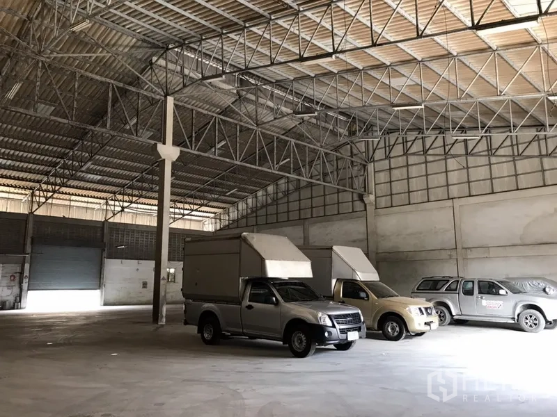 Warehouse for rent in Mueang Samut Prakan, Samut Prakan - Interior view toward roller shutters with steel truss ceiling, smooth concrete floor, and ample vehicle space.