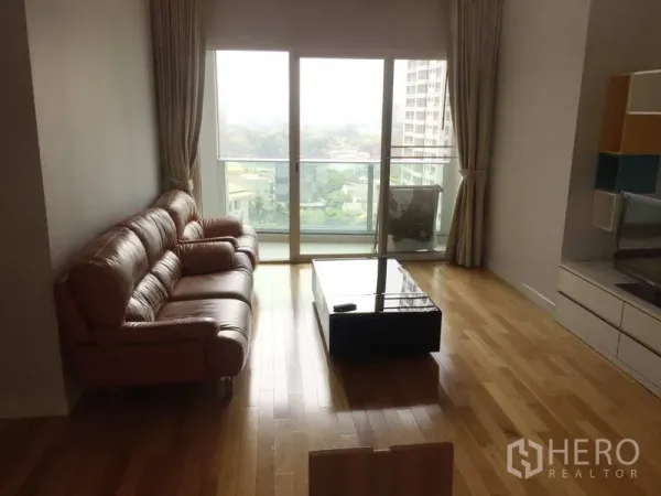 Condominium for sale in Khlong Toei, Bangkok - Living area opening to a balcony with city view through full-height sliding glass doors.