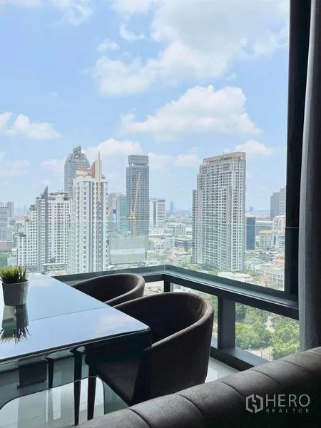 คอนโด ให้เช่าในBang Rak, Bangkok - โต๊ะทานอาหารกระจกกับเก้าอี้บุนุ่มริมหน้าต่าง มองเห็นตึกสูงของกรุงเทพฯ