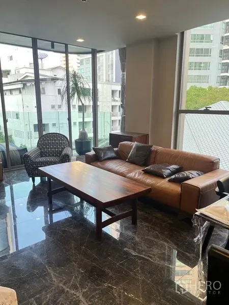 公寓 出租在Watthana, Bangkok - 客厅配皮质沙发与木质茶几，黑色大理石地面，落地窗眺望城市景观