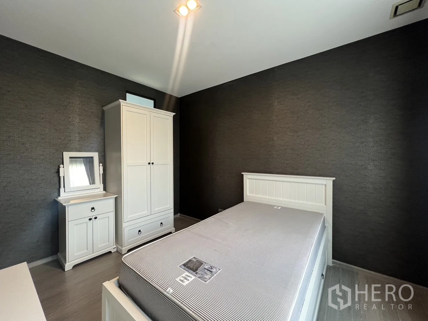 Townhouse for rent in Lat Phrao, Bangkok - Guest bedroom with white bed set, wardrobe and dressing table against dark feature wall.