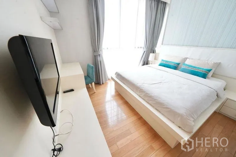 Condominium for rent or sale in Watthana, Bangkok - Sunlit bedroom with king bed, wall-mounted TV and full-height windows with curtains.