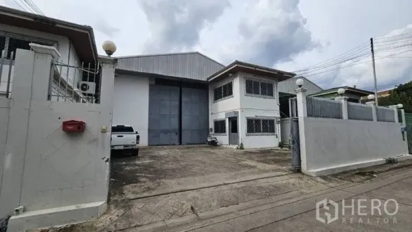 Warehouse for rent in Lak Si, Bangkok - Gated warehouse exterior with wide industrial entry door, driveway parking, and two-storey office.