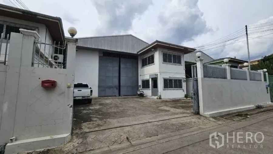 Warehouse for rent in Lak Si, Bangkok - Gated warehouse exterior with wide industrial entry door, driveway parking, and two-storey office.