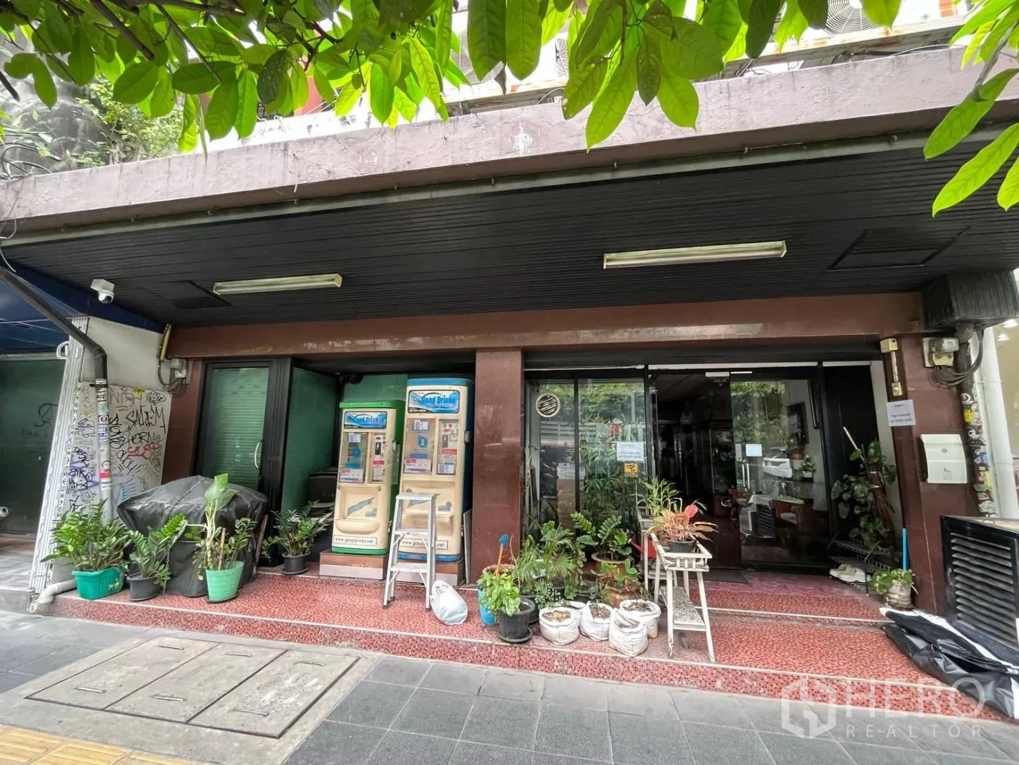 Shophouse for rent in Khlong Toei, Bangkok - Street-front shophouse facade with glass doors, awning, vending machines, and potted plants.
