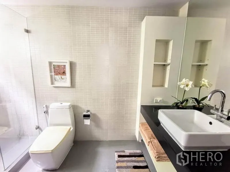Detached House for rent or sale in Bang Phli, Samut Prakan - Bright bathroom with glass shower, wall niches, square basin on black countertop and toilet.