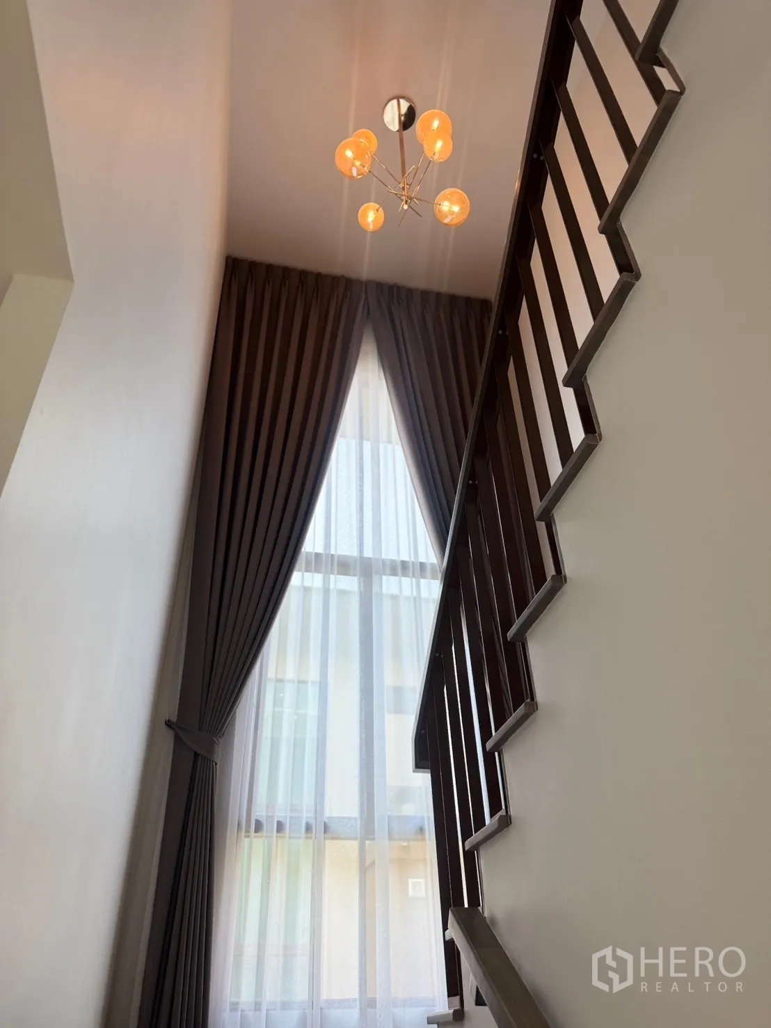 Detached House for rent or sale in Bang Kapi, Bangkok - Staircase with a tall window, sheer curtains and a modern pendant light.
