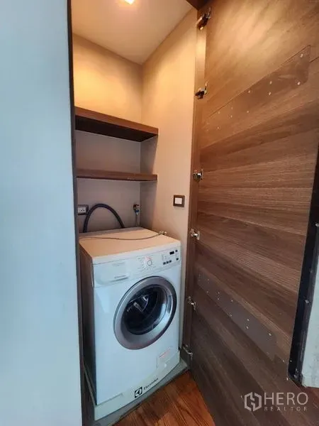 Condominium for rent in Bang Rak, Bangkok - Compact laundry closet with a front‑loading washing machine and built‑in shelves.