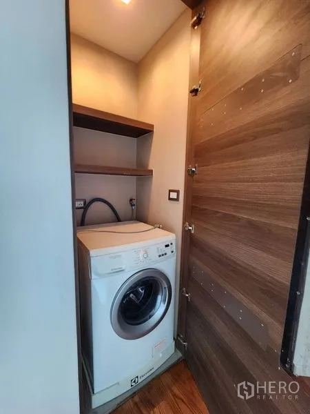 Condominium for rent in Bang Rak, Bangkok - Compact laundry closet with a front‑loading washing machine and built‑in shelves.