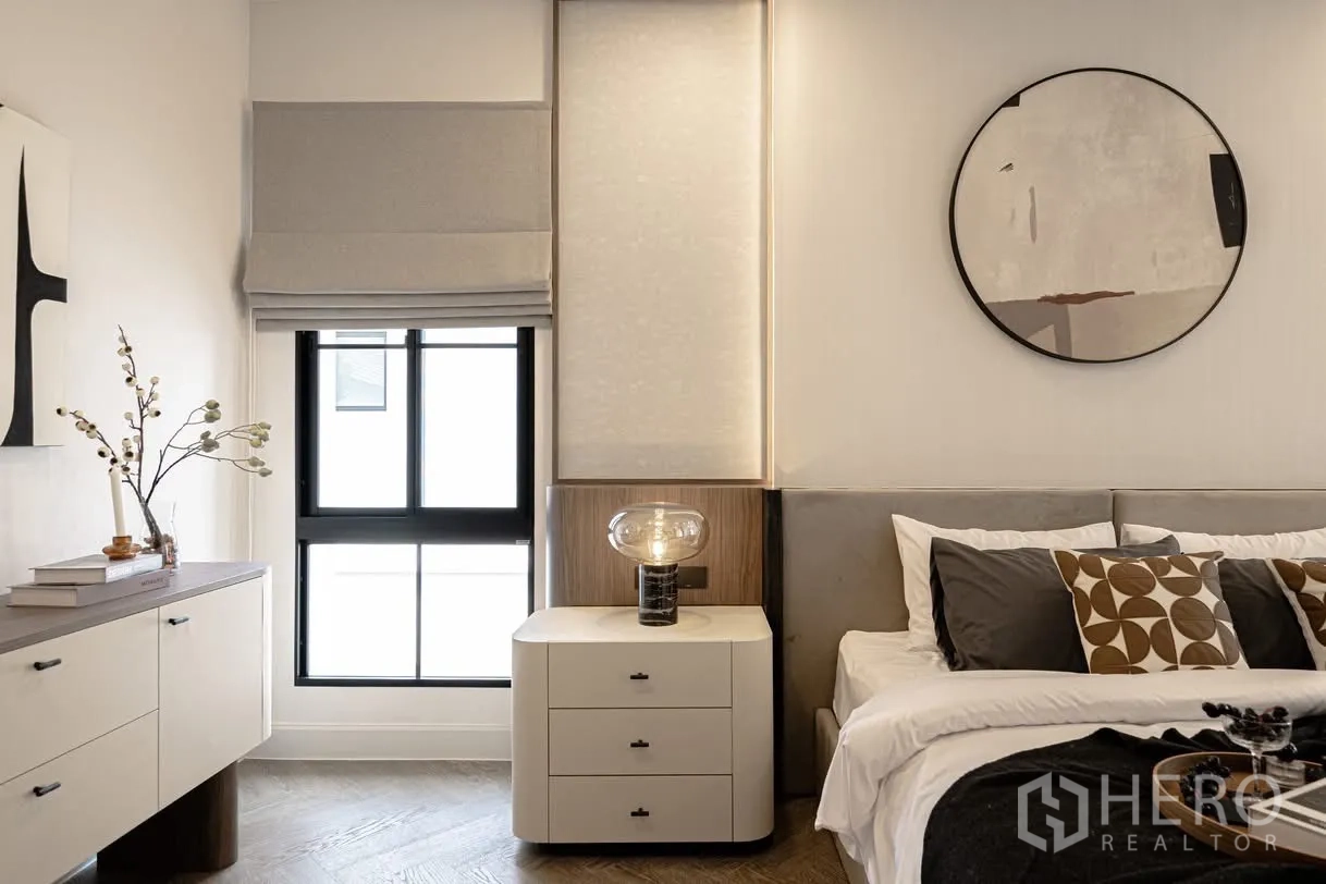 Detached House for rent in Saphan Sung, Bangkok - Bedside table with glass lamp beside window with Roman shade and dresser in a bright bedroom.