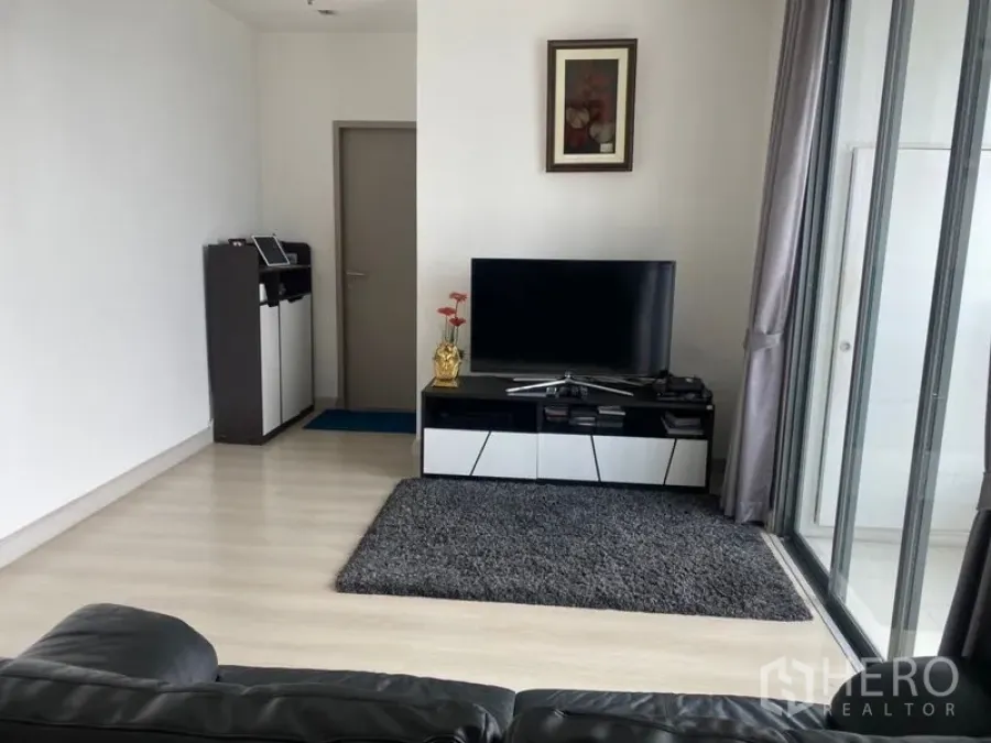 Condominium for sale in Phra Khanong, Bangkok - Bright living room with TV console, rug and floor-to-ceiling glass doors to the balcony