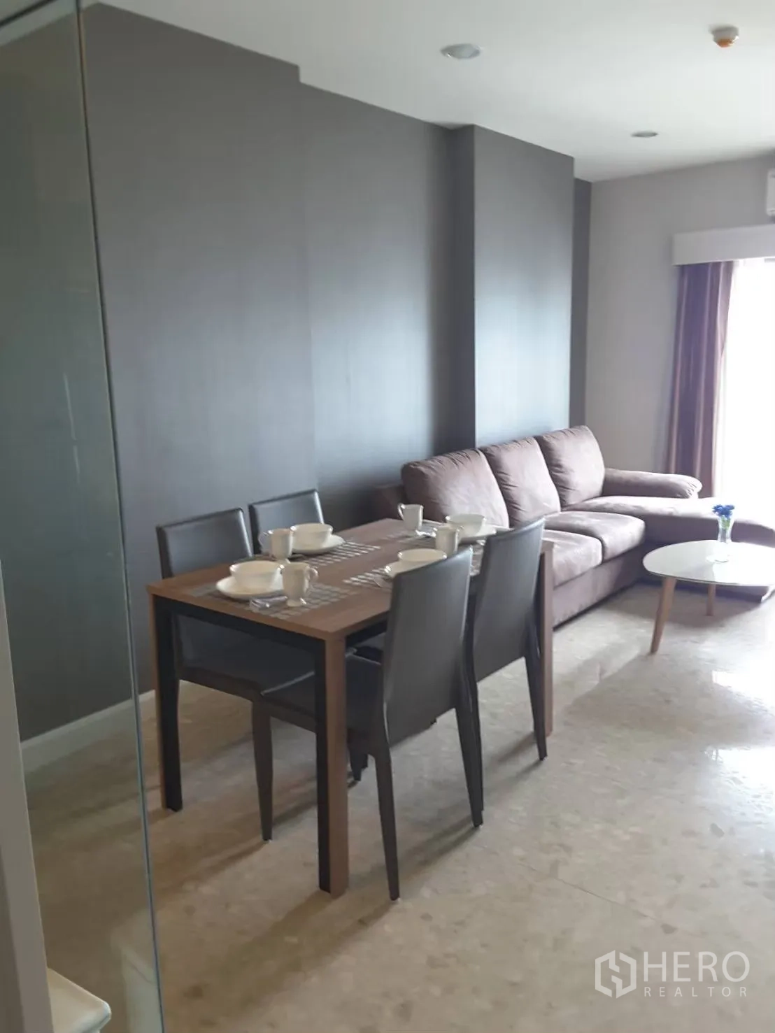 Condominium for rent in Khlong Toei, Bangkok - Four-seat dining table beside a gray feature wall and sofa.