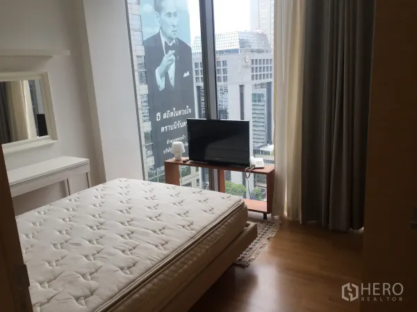 Condominium for rent in Bang Rak, Bangkok - Bedroom with large window and skyline view, wood floors, and a compact TV stand.