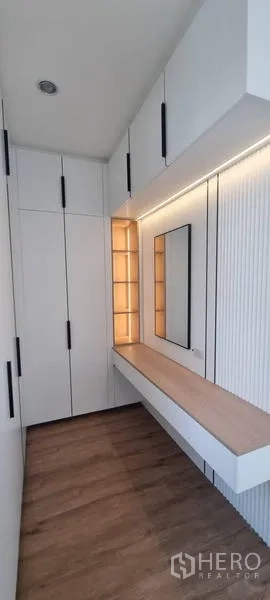 Detached House for rent in Saphan Sung, Bangkok - Built-in white wardrobes with a vanity desk, mirror, and warm accent lighting over wood flooring.