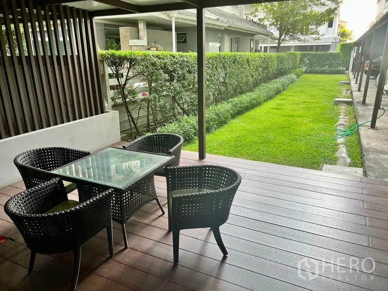 Condominium for rent in Bang Kho Laem, Bangkok - Covered outdoor terrace with rattan dining set overlooking a manicured lawn and hedge.