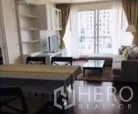 Condominium for rent in Watthana, Bangkok - Living area angle showing TV stand, dining set and large windows to the balcony.